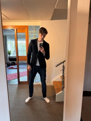 Mörkblå slim fit kavaj herr (J-lindeberg) - Stilren svart kavaj i slim fit-modell med klassisk krage och två knappar framtill. Långa ärmar och figurnära passform ger en modern look. Perfekt att matcha med jeans eller chinos för en snygg outfit.