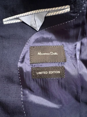 Mörkblå kavaj från Massimo Dutti - Snygg mörkblå kavaj från Massimo Dutti Limited Edition. Klassisk passform med smala slag och innerficka med ljusblå detalj. Perfekt för dig som vill ha en stilren och exklusiv look. Materialet känns lyxigt och kavajen har en elegant finish.