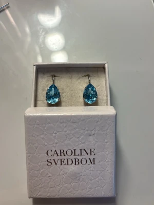 Blå droppformade örhängen Caroline Svedbom - Snygga örhängen från Caroline Svedbom med stora, droppformade blå kristaller. Örhängena har silverfärgade detaljer och klassisk stängning. Perfekta för att ge din look lite extra färg och glans. pris kan diskuteras 💛
