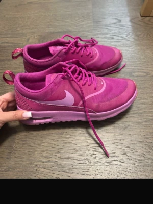 Nike rosa sneakers med meshdetaljer - Snygga rosa Nike sneakers med vit swoosh och meshdetaljer på ovandelen. Skorna har klassisk låg profil, snörning och en bekväm sula med synlig Air Max-dämpning. Perfekta för dig som gillar färg och sportig stil. Lite smutsiga men inga skavanker 