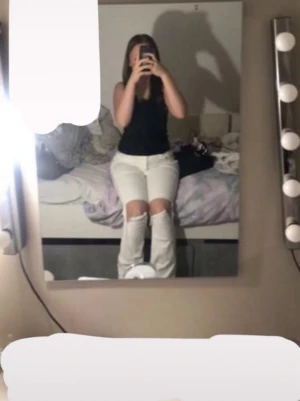 Vita ripped jeans med hål på knäna - Säljer ett par vita jeans med utsvängda ben och stora hål över knäna. Jeansen har klassisk femficksdesign och låg midja. Perfekta för dig som gillar en trendig och avslappnad stil.