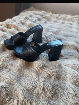 Svarta platå klackar  - Snygga svarta klackar med hög platåklack. Skorna har öppen tå, bred rem över foten och fyrkantig tåform. Tillverkade i ett glansigt syntetmaterial som ger en trendig look. Perfekta för att lyfta din outfit med extra höjd. Lite smutsiga men går att tvätta. 