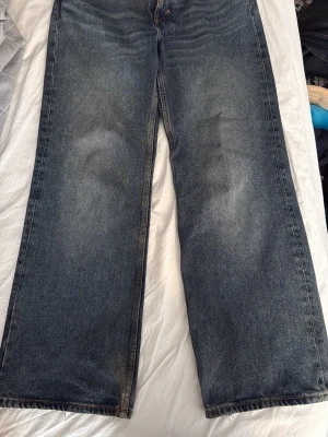 Blåa baggy jeans  - Säljer ett par klassiska blå jeans med rak och bred passform från monki. Jeansen har hög midja, men man kan dra ner dom till höften för low waist look. Perfekta för en avslappnad och trendig look. Storlek 28/32. De är lite slitna nertill.