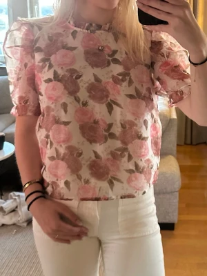 Blommig puffärm blus i rosa toner - Söt blus med puffiga korta ärmar och blommigt mönster i rosa och beige toner. Blusen är lätt transparent och har en rak passform med voluminösa axlar. Perfekt för dig som gillar romantisk och trendig stil.