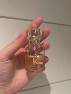 Kérastase Le Parfum glasflaska - Kérastase Le Parfum i en stilren, genomskinlig glasflaska med silvrig kork. Parfymen har en ljus bärnstensfärgad vätska och flaskan är kompakt och rundad med elegant design. Perfekt för dig som gillar lyxiga dofter.
