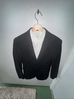 Svart kavaj från Selected Homme - Stilren svart kavaj från Selected Homme med klassisk passform och två knappar framtill. Perfekt till skjorta och passar till många olika tillfällen. Enkel design utan mönster och med snygg krage.