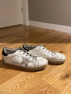 Golden Goose Superstar vita sneakers - Golden Goose Superstar sneakers i vitt läder med grå en stjärna på sidan. Skorna är storlek 39. Priset går att diskutera hör av dig vid minsta fråga.