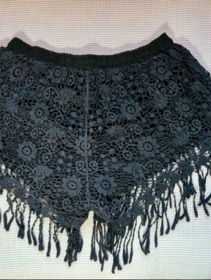 Svarta virkade spetsshorts med fransar – Festival/Boho Style - Superfina svarta korta shorts i boho-stil med vacker virkad spets och dekorativa fransar nertill. Shortsen är vintage, köpta i Thailand för ca 20 år sedan, och saknar storlekslapp. Små i storleken, passar bäst XS eller en liten S. De har bekväm resår i midjan och ett tunt fodertyg. Observera att de är något genomskinliga (visas på sista närbilden). Perfekta för sommaren, stranden eller festivaler! Skick: Mycket gott skick för sin ålder. Midja: ca 62 cm (ej utsträckt). Längd: ca 20 cm.