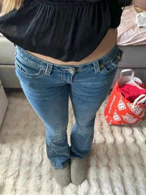 True religion bootcut low waist jeans - Snygga blå bootcut jeans med låg midja och klassiska fem fickor. Jeansen har en lätt tvättad look och sitter tajt över låren för att sedan bli vidare nedtill. Perfekta för en trendig och avslappnad stil. Orginal pris 1799, fråga om mått för tycker inte storleken stämmer överens, står 29 men borde stå en större storlek 