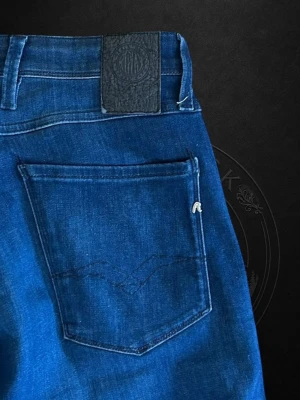  Replay Anbass - Snygga blå slim fit jeans från Replay med klassisk femficksdesign och diskret logotyp på bakfickan. Jeansen har en mörk tvätt och är tillverkade i mjukt denimtyg med stretch för extra komfort. Perfekta för en trendig och avslappnad look.