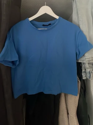 Blå croppad t-shirt - En enkel blå croppad t-shirt med rund hals och korta ärmar. T-shirten har en avslappnad passform och är tillverkad i mjuk bomull, perfekt för en chill och stilren look. 