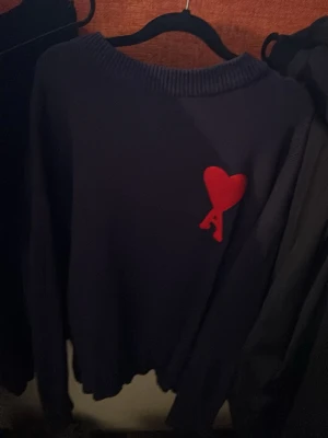 Ami Paris tröja mörkblå - Snygg mörkblå stickad tröja med ett rött hjärta och bokstaven A broderat på bröstet. Tröjan har rund halsringning och långa ärmar. Perfekt för dig som gillar stilrena plagg med en twist. Ami Paris tröja jätte bra skick skickar samma dag! Den passar även folk med M