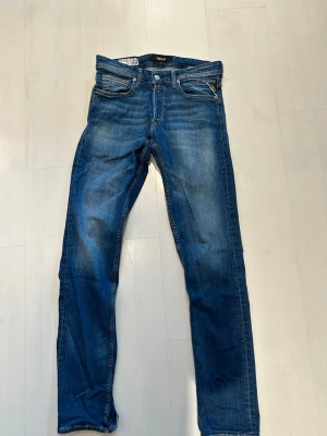 Blå jeans från Replay med slitningar - Säljer ett par blå jeans från Replay med snygga slitningar och tvättade detaljer. Klassisk femficksmodell med dragkedja och knapp i midjan. Jeansen har raka ben och är tillverkade i denim med en cool vintage-look.modell Grover, storlek W32 L34.