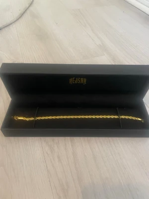 Guldfärgat armband från kejsar - Snyggt guldfärgat armband från Hejsar med tvinnad kedja. Armbandet har en stilren och klassisk design som passar perfekt till din vardagsstil. Levereras i en elegant svart ask med guldfärgad logga.