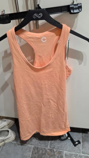 Persikofärgad linnetopp i bomull - Snygg persikofärgad linnetopp från C Organic Cotton i mjuk bomull. Modellen är ärmlös med klassisk racerback och har en enkel, stilren design som passar perfekt till sommaren.