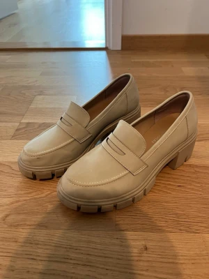 Chunky beige loafers från Sincerely Jules - Snygga chunky loafers i beige från Sincerely Jules. Skorna har en kraftig sula med grovt mönster och klassisk pennyloafers-design. Tillverkade i slätt material med stilren look och rundad tå. Perfekta för dig som vill ha en trendig och bekväm sko till vardags. Endast använda en gång. 
