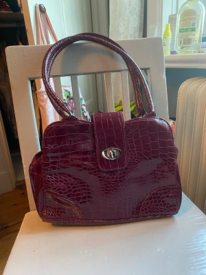Mörk rosa handväska med aligator mönster - Super snygg glansig mörk rosa väska med aligator mönstrad tyg❤️den är 28cm bred och 22cm hög och bandet är 50 cm