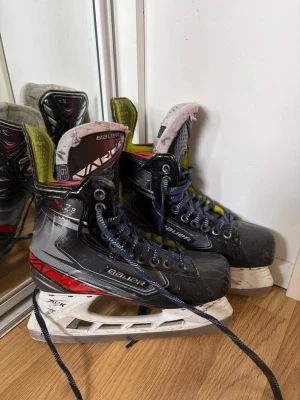 Bauer Vapor X2.9 hockeyskridskor - Säljer ett par Bauer Vapor X2.9 hockeyskridskor i svart med röda och gula detaljer. Skridskorna har blå snören, stabil konstruktion och klassisk design för hockey. Perfekta för dig som vill ha bra grepp och kontroll på isen.