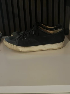 Svarta låga sneakers i läder - Stilrena svarta sneakers från Lanvin med lågt skaft och vita sulor. Skorna har svarta skosnören, metallöljetter och är tillverkade i läder. Perfekta för en clean och enkel look. Storlek 44 men passar 45 (OBS! Lådan medföljer ej)