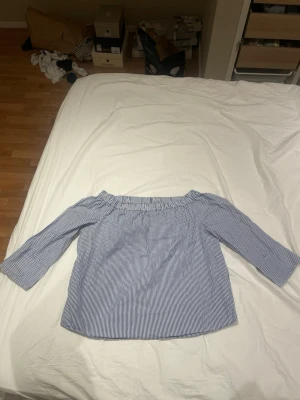 Blårandig offshoulder blus - Snygg blårandig offshoulder blus med trekvartsärm. Blusen har tunna vita och blå ränder och en elastisk kant upptill som gör att den sitter bra över axlarna. Perfekt till jeans eller kjol för en fräsch look. Materialet känns lätt och luftigt.