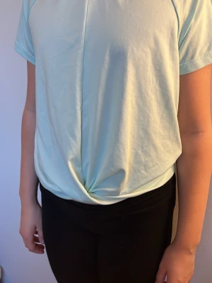 Ljusblå twistad tränings tröja  - Snygg ljusblå t-shirt med kort ärm och twistad detalj framtill. T-shirten har en rak passform och är tillverkad i mjukt bomullstyg. Perfekt tränings T-shirt i storlek 158-164