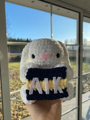 Virkad AIK-kanin  - Söt handvirkad kanin i mjukt vitt garn som håller en AIK flagga. Perfekt för AIK-supportern som gillar unika prylar.