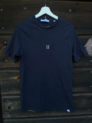 Svart t-shirt från Les Deux - Snygg svart t-shirt från Les Deux med enkel design och stilren logga tryckt på bröstet. Klassisk passform och rund halsringning. Perfekt till jeans eller shorts för en clean look.