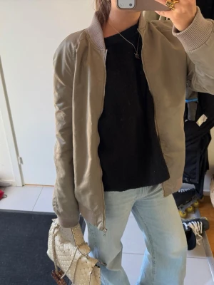 Khaki bomberjacka med ribbade muddar - Snygg khaki bomberjacka med dragkedja framtill och ribbade muddar vid ärmslut och krage. Köpt second hand !!