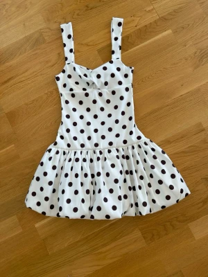  Ny trendig Vit klänning med svarta prickar - Supersöt vit kortklänning med svarta prickar och breda axelband. Klänningen har en lätt utställd kjol och markerad midja, perfekt för en trendig och lekfull look. Materialet känns mjukt och svalt, perfekt för varmare dagar. Egna bilder på annonsen 