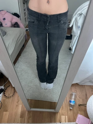 Svarta bootcut jeans med kontrastsömmar - Säljer ett par svarta bootcut jeans med snygga kontrastsömmar och klassisk femficksdesign. Jeansen har låg midja och är i stretchigt material som sitter tajt upptill och släpper ut vid benen. Perfekta för en trendig och avslappnad look.
