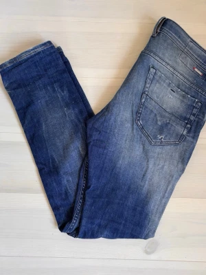 Diesel Jeans - Säljer ett par blå jeans från Diesel med slitningar. Jeansen ha smal passform. Perfekta för en avslappnad och trendig look. Storlek W31 L32