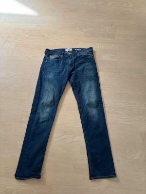 Blå jeans från Replay - Snygga blå jeans från Replay med klassisk femficksdesign och raka ben. Jeansen har lätt slitna detaljer på låren och är tillverkade i bomull. Perfekta för en avslappnad och trendig stil.