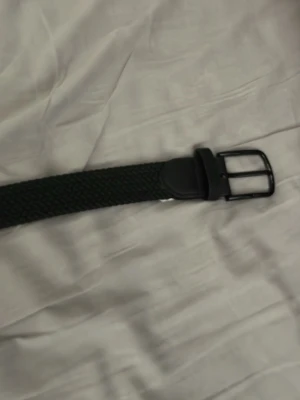 Svart flätat bälte med metallspänne - Stilrent svart bälte med flätad design och klassiskt metallspänne. Perfekt accessoar för att lyfta din outfit. Bältet är flexibelt och passar till många olika stilar.