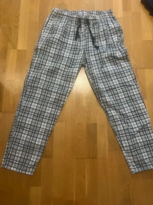 Rutiga pyjamasbyxor i bomull - Mysiga pyjamasbyxor med gråvitt rutmönster och justerbar midja med snörning. Tillverkade i mjuk bomull, perfekta för chillkvällar hemma. Byxorna har sidofickor och avslappnad passform.