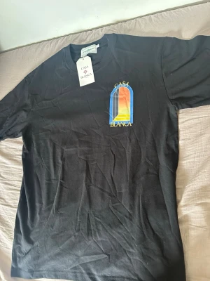 Svart t-shirt från Casablanca - Svart t-shirt från Casablanca med färgglatt tryck på bröstet och rund halsringning. T-shirten har en klassisk passform och är tillverkad i mjuk bomull. Perfekt för en stilren och trendig look.