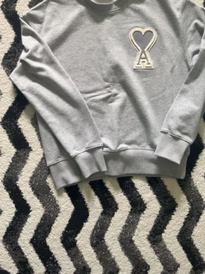 sweatshirt Ami Paris - Snygg grå sweatshirt från Ami Paris med det ikoniska hjärta-A broderiet på bröstet. Tröjan har rund hals, ribbade muddar och är tillverkad i mjuk bomull. Perfekt för en avslappnad och trendig look.