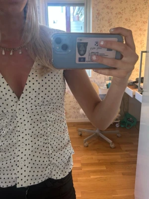 Vit prickig blus med knappar - Snygg vit blus med svarta prickar och v-ringning. Blusen har knappar framtill och korta ärmar med lätt volang. Perfekt för dig som gillar en klassisk men trendig look.