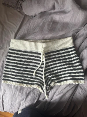 Randiga stickade shorts med snörning - Mysiga stickade shorts med svartvita ränder och bred ribbad midja. Shortsen har snörning framtill och är perfekta för en avslappnad stil. Materialet är mjukt och stretchigt, vilket gör dem riktigt bekväma att bära.