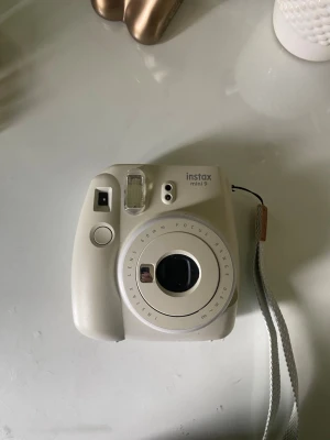 Vit Instax Mini 9 digitalkamera - Säljer en vit Instax Mini 9 från Fujifilm. Kameran har en kompakt och rundad design i plast, inbyggd blixt och enkel knapp för att ta bilder. Perfekt för att ta direktbilder och har en praktisk handledsrem.