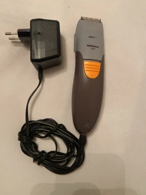 Philips Philishave hårtrimmer - Philips Philishave C482 hårtrimmer i grå och orange plast med metallblad. Kommer med laddare och lång sladd. Ergonomiskt handtag och tydlig på/av-knapp. Perfekt för att trimma hår eller skägg hemma.
