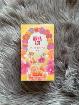 Anna Sui Fairy Dance Sun parfym - Anna Sui Fairy Dance Sun parfym i en färgglad kartong med blommor och älvor. Förpackningen är gul, rosa och orange med lekfull design. Volymen är 50 ml och parfymen tillhör Secret Wish-serien.