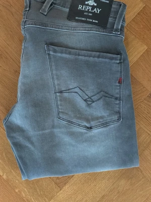 Grå slim jeans från Replay - Snygga grå jeans från Replay med klassisk femficksdesign och diskret logga på bakfickan. Jeansen har en slim passform och är tillverkade i mjuk bomull med lite stretch för extra komfort. Perfekta till en avslappnad streetstyle-look.