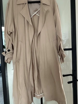 Beige trenchcoat Zara - Stilren beige trenchcoat. Ärmarna har snygga spänndetaljer med knappar. Perfekt för lager-på-lager och en tidlös look.