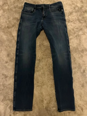 Mörkblå slim fit jeans från Replay - Snygga mörkblå slim fit jeans från Replay med klassisk femficksdesign och diskreta slitningar. Jeansen har en smal passform och är tillverkade i stretchigt denimtyg för extra komfort. Perfekta för en trendig och avslappnad stil.