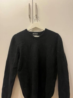 Svart cashmere tröja från Autograph - Klassisk svart stickad tröja från Autograph med V-ringning. Tröjan har lång ärm och är tillverkad i en mjuk ullblandning som känns både stilren och bekväm. Perfekt för lager-på-lager och enkel att matcha med olika outfits.
