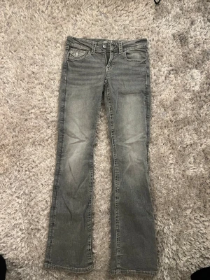 Grå bootcut jeans  - Snygga grå jeans med bootcut-modell. Klassisk femficksdesign och knappgylf. Jeansen har en tvättad look och raka ben som blir lite utsvängda nertill. Perfekta för en avslappnad och trendig stil.