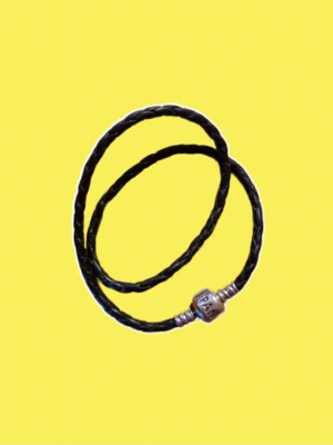 Svart flätat Pandora armband - Snyggt svart flätat armband från Pandora med ett klassiskt silverlås där Pandora-loggan är ingraverad. Armbandet är gjort av läder och kan bäras både enkelt eller med berlocker för en personlig stil.