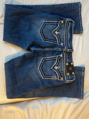 Mörkblå bootcut jeans Miss Me - Snygga mörkblå bootcut jeans från Miss Me med kontrastsömmar och klassisk femficksdesign. Jeansen har dekorativa detaljer vid fickorna och är tillverkade i denim med lätt stretch för skön passform. (De säljs inte längre men fick de av mamma)