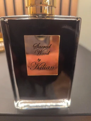 Sacred Wood by Kilian parfym - Lyxig parfymflaska från Kilian i svart glas med guldfärgad etikett och lock. Doften heter Sacred Wood  Provsprayad Full EJ BOX