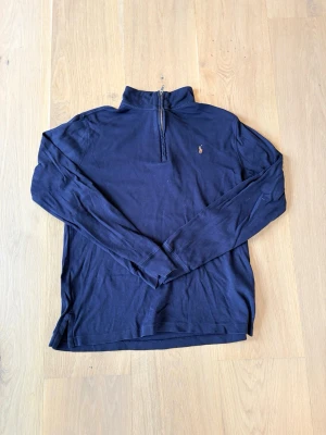 Mörkblå halvzip från Polo Ralph Lauren - Mörkblå långärmad tröja från Polo Ralph Lauren med halv dragkedja och liten broderad logga på bröstet. Tröjan har hög krage och är tillverkad i ett mjukt, tunt material som passar perfekt till lager på lager. Klassisk och stilren design.                        Hör av dig vid minsta fundering😊